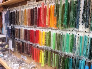 Strings of beads for sale arranged by color inside Beads by the Bay.
